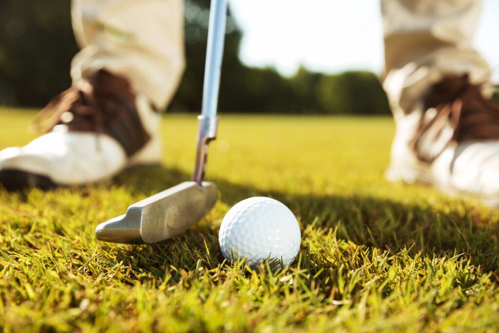 Golfer preparing to putt on a sunny golf course with a close-up of the golf ball and putter on green grass.