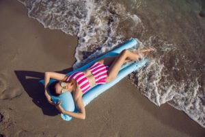Woman in striped bikini relaxing on blue float as ocean waves roll in