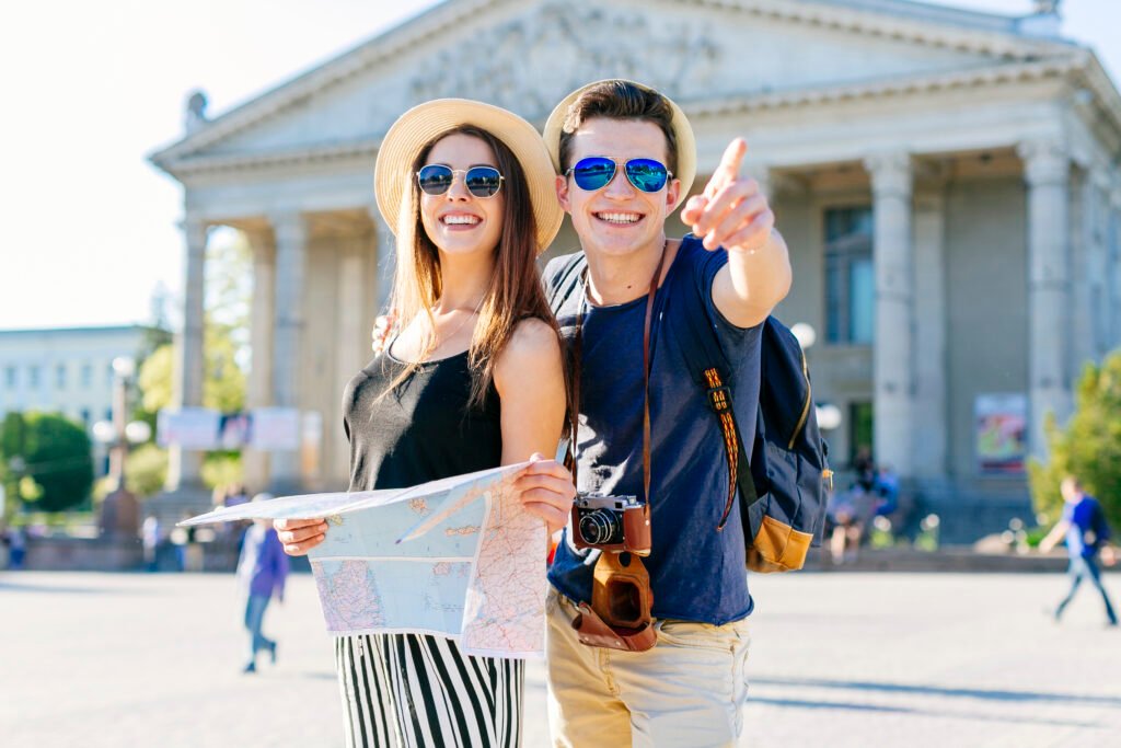 Smiling couple holding a map and pointing at a landmark in front of a historic building, enjoying a sunny day in the city.
