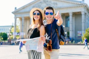 Smiling couple holding a map and pointing at a landmark in front of a historic building, enjoying a sunny day in the city.