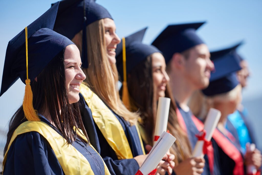 Smiling graduates in caps and gowns holding diplomas outdoors